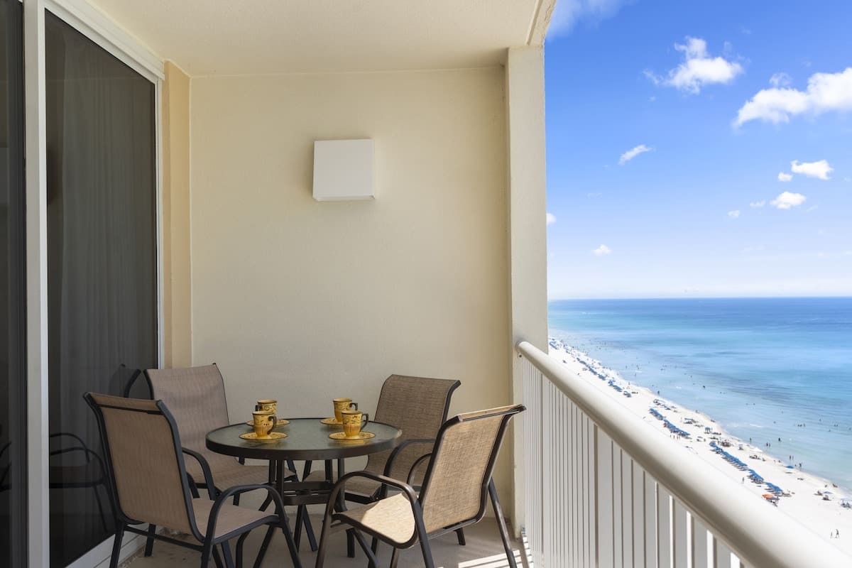 Majestic T2 - 1606 – Balcony with a glass table and four chairs, overlooking a beach and ocean view.