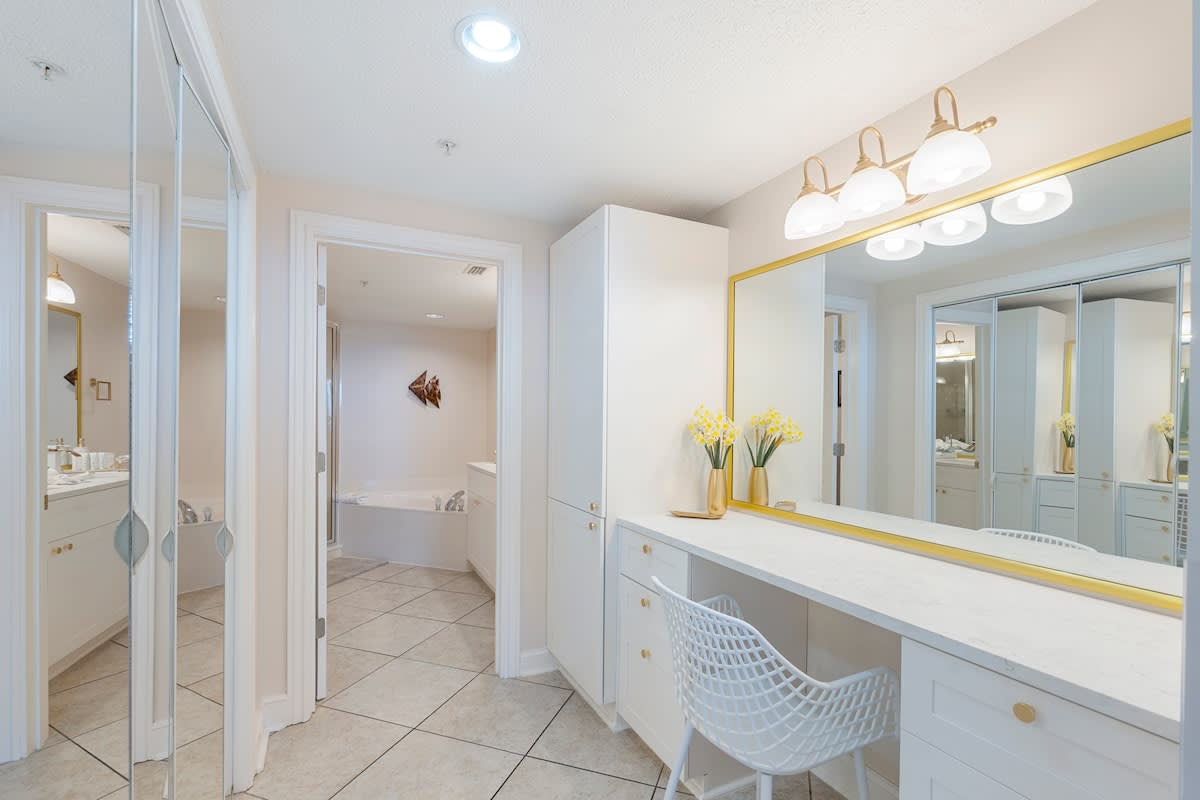 Majestic T2 - 1606 – Bright bathroom with double sinks, large mirror, decorative flowers, and a view of a separate tub.