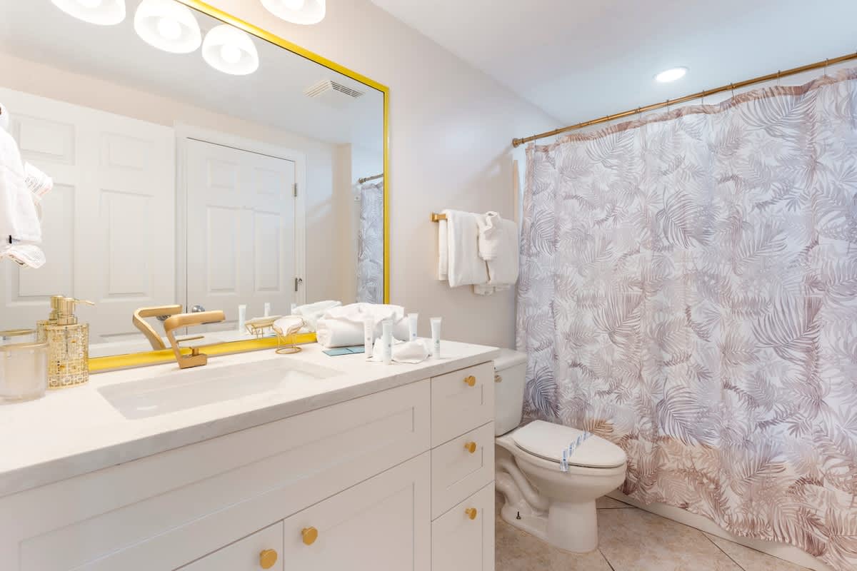 Majestic T2 - 1606 – Bright bathroom with a sink, mirror, shower curtain, and toilet, featuring a light color scheme.