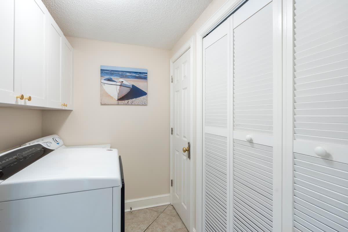 Majestic T2 - 1606 – Laundry room with washing machine, white cabinets, and a beach-themed wall art.