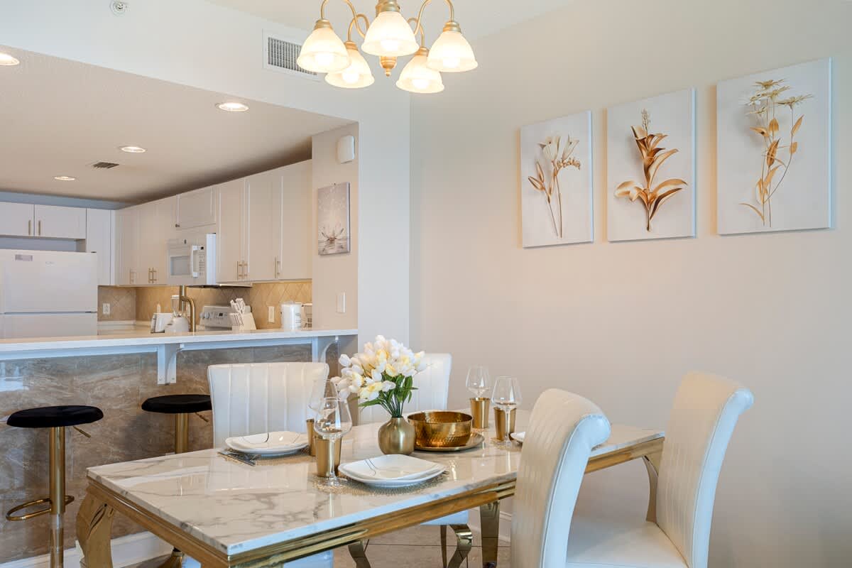 Majestic T2 - 1606 – Bright dining area with a marble table, white chairs, and an open kitchen view.