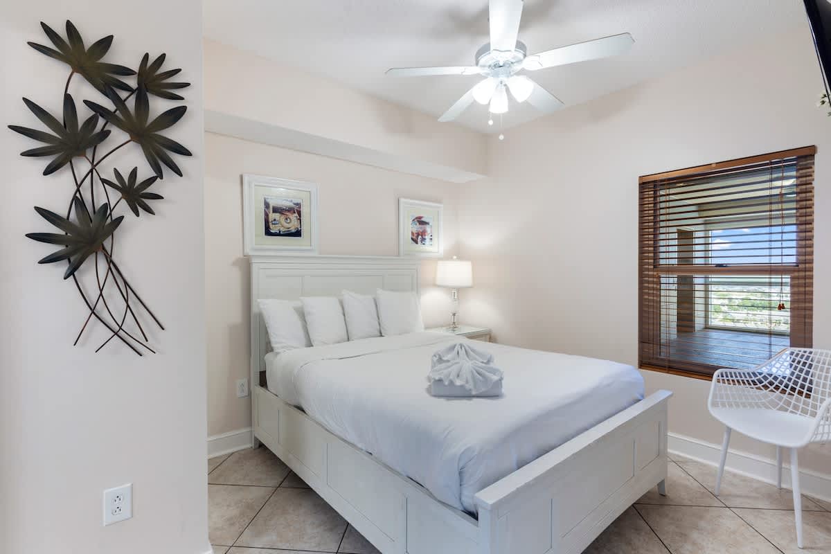 Majestic T2 - 1606 – Bright bedroom with a queen bed, ceiling fan, window blinds, and decorative wall art.