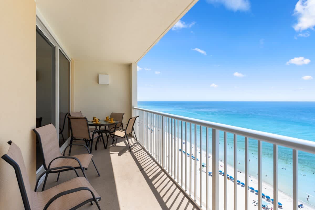 Majestic T2 - 1606 – Balcony with chairs and table overlooks beach and ocean with blue sky.