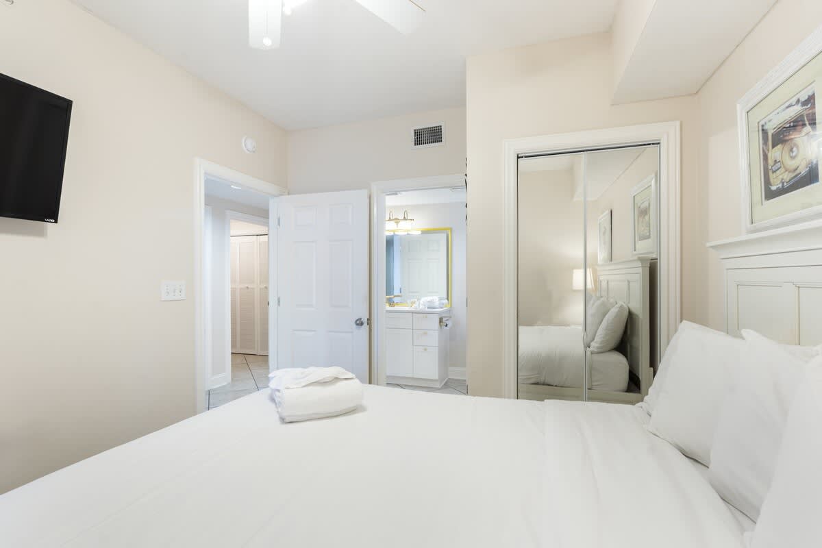 Majestic T2 - 1606 – Bedroom with a bed, TV, mirror closet, and bathroom doorway.