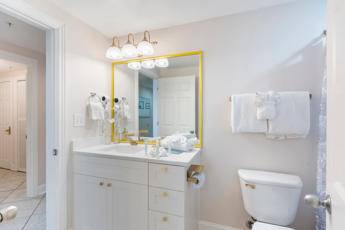 Majestic T2 - 1606 – Bright bathroom with a sink, golden fixtures, and a large mirror featuring a yellow frame.