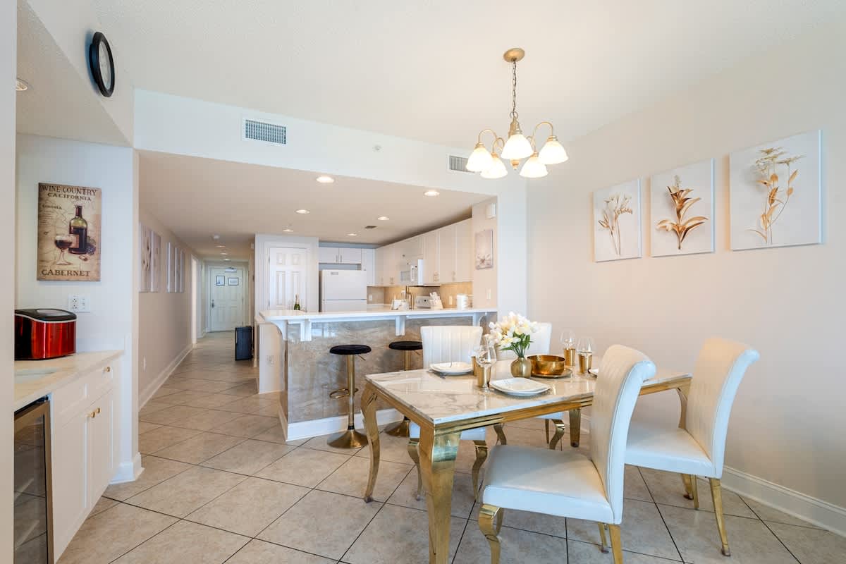 Majestic T2 - 1606 – Bright dining area with a glass table, gold accents, and modern kitchen bar stools.