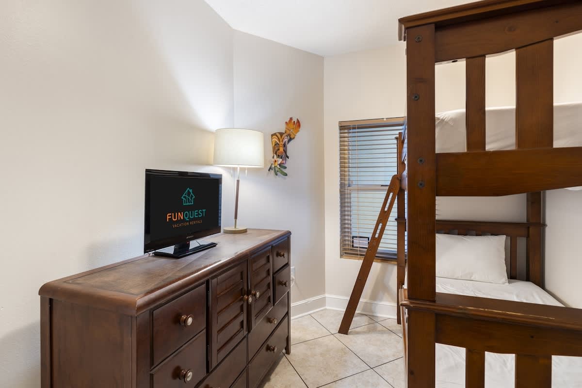Majestic T2 - 1606 – Cozy room with a wooden dresser, TV, lamp, and a bunk bed near a window.