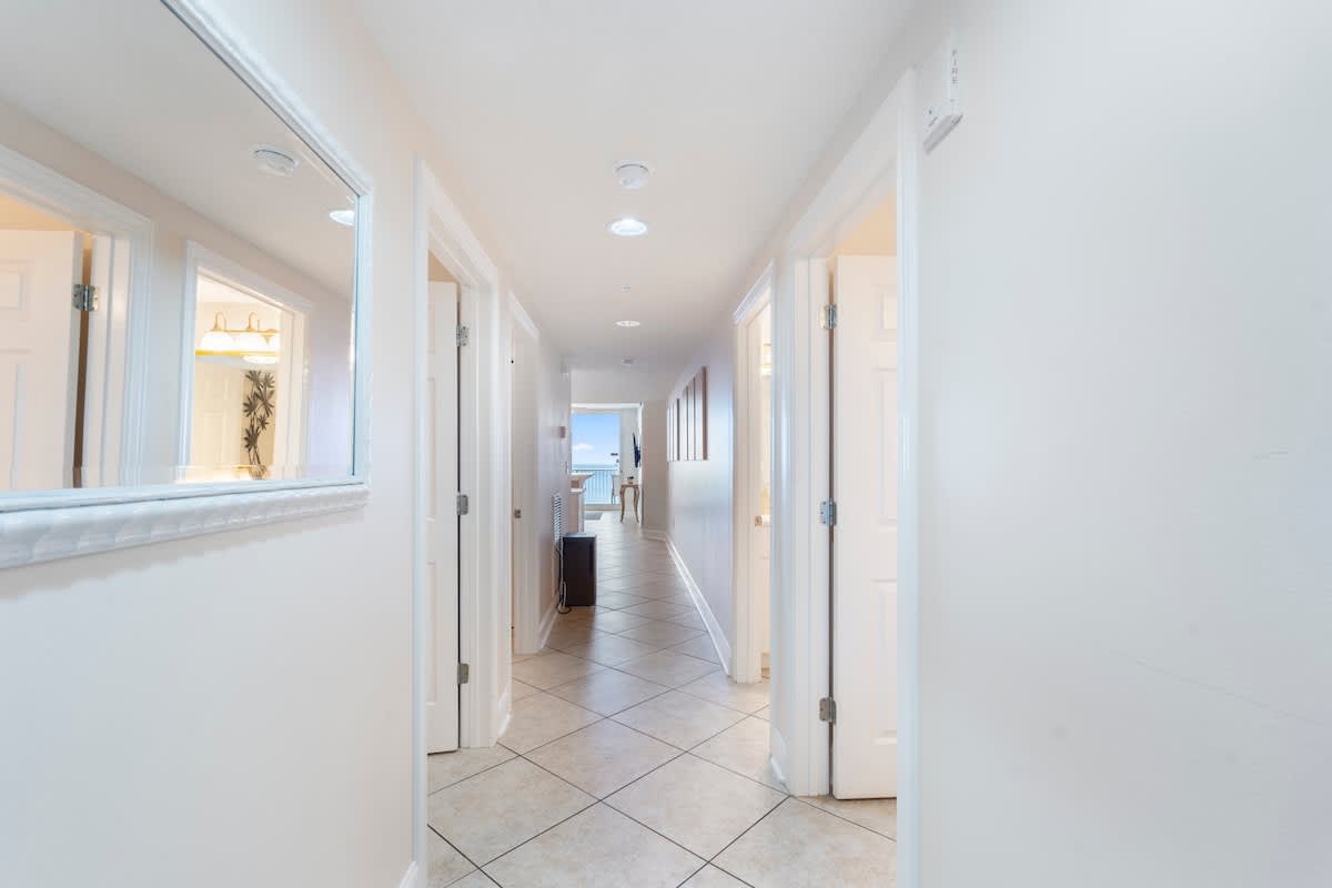 Majestic T2 - 1606 – Hallway with doors to rooms, tile floor, and view of living area and balcony at the end.