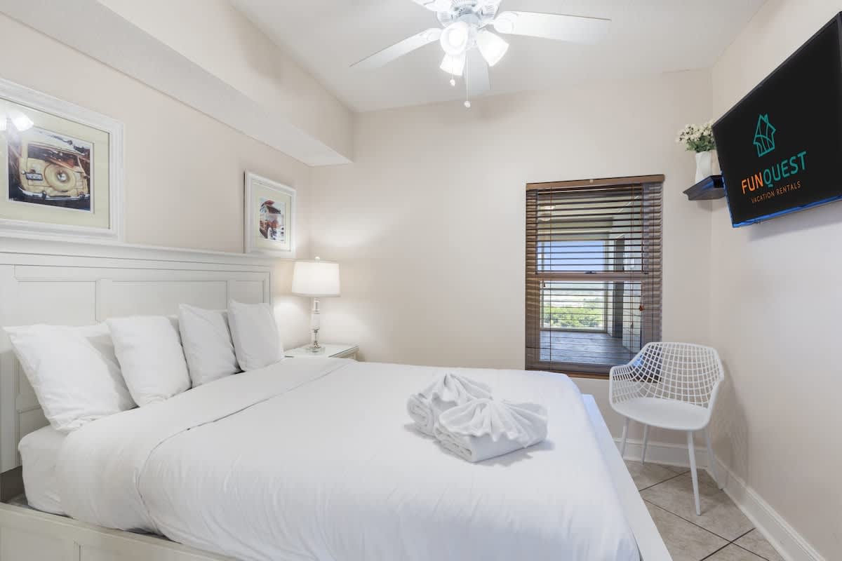 Majestic T2 - 1606 – Cozy bedroom with a queen bed, artwork, lamp, TV, and window view.