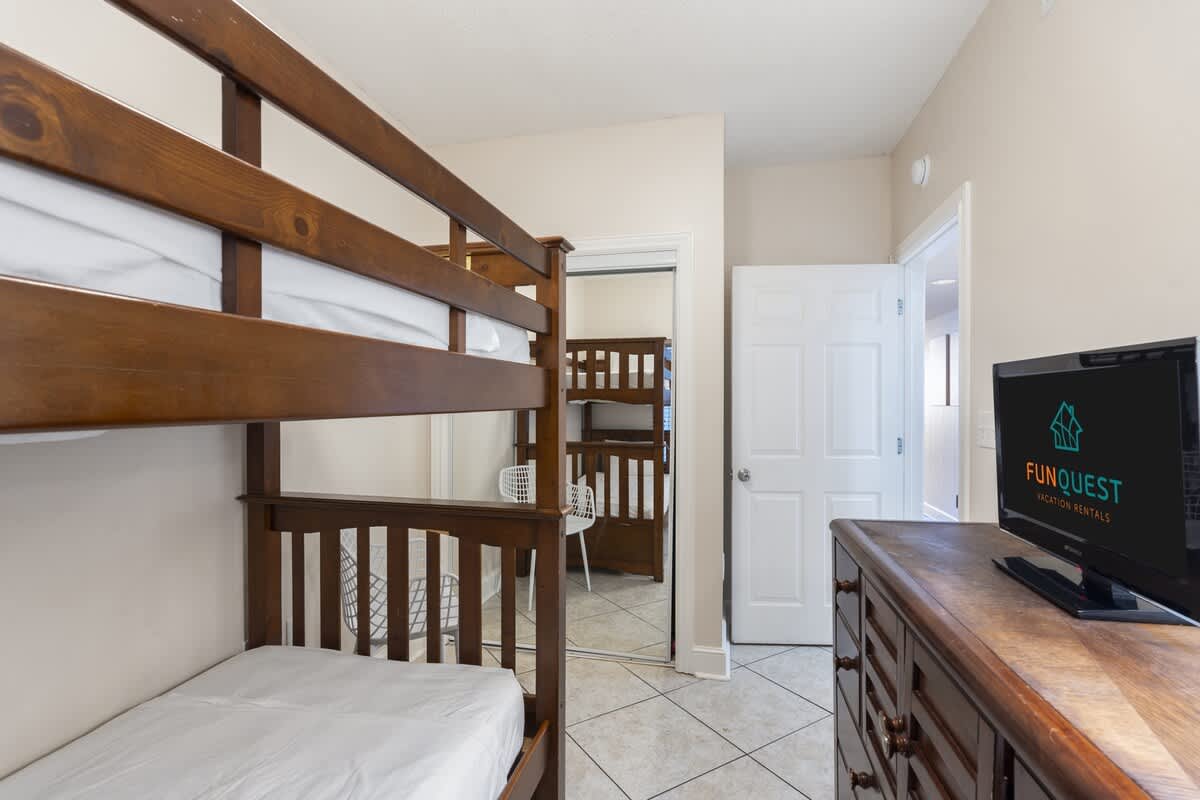 Majestic T2 - 1606 – Bunk room with wooden bunk beds, dresser, and TV, featuring tile flooring and light walls.
