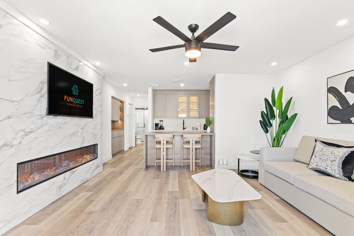 Ocean Breeze 4A – Modern living room with a couch, TV, kitchen bar, and decorative plants.