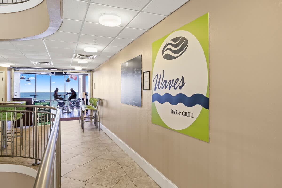 Tidewater 2615 – Interior hallway featuring the Waves Bar & Grill sign, with a view of the ocean and seating area.