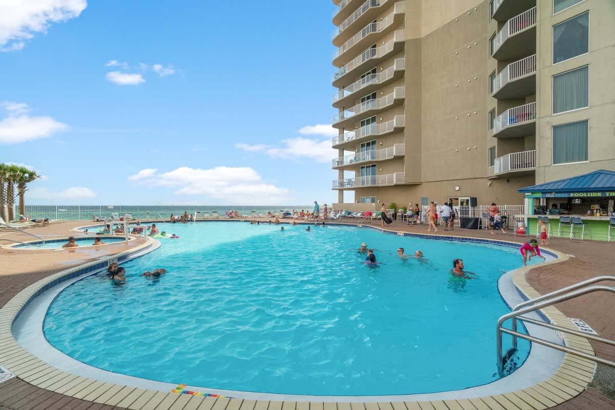 Tidewater 2615 – Pool area with swimmers, sun loungers, and a view of the ocean and building balconies.