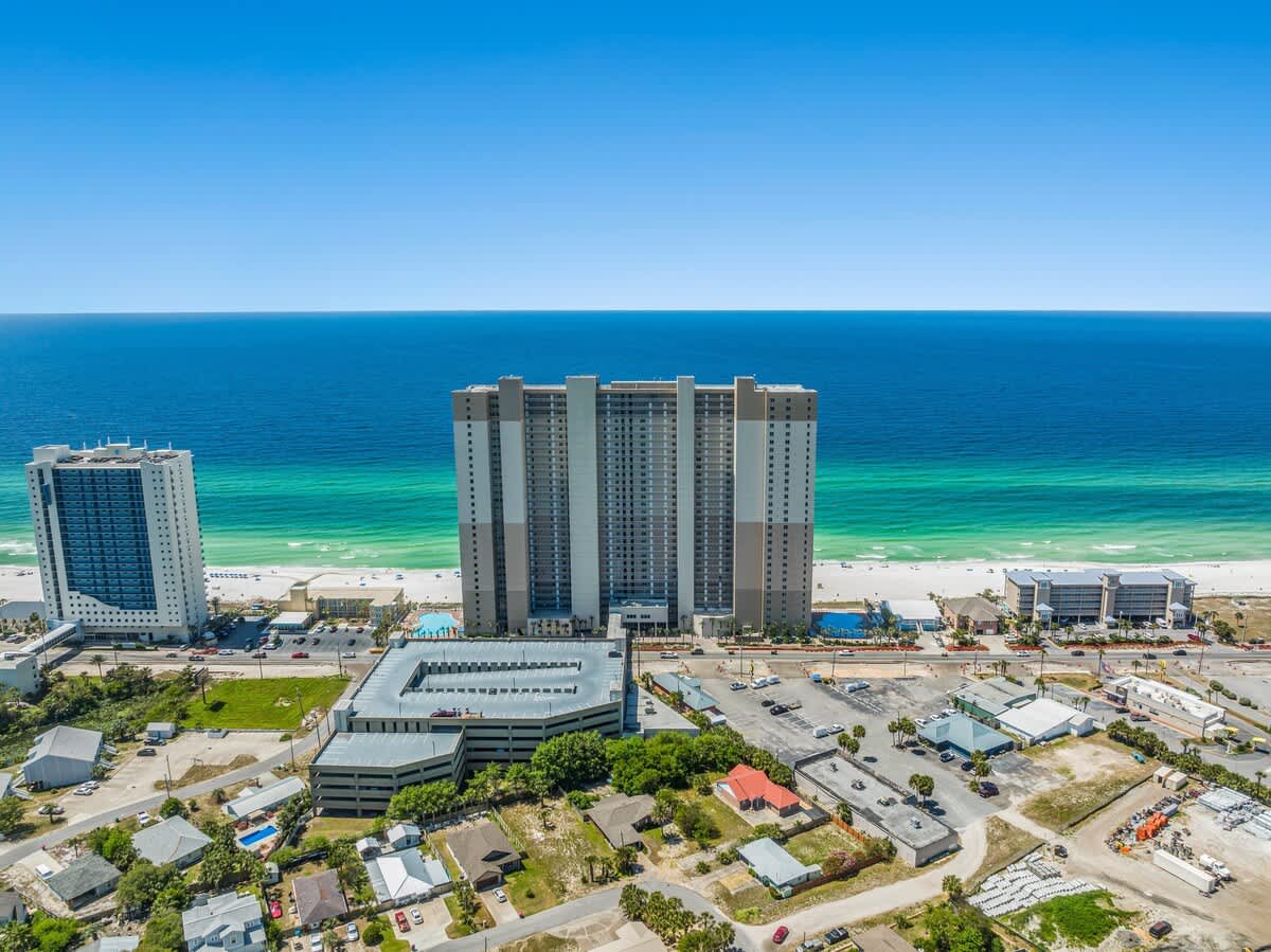 Tidewater 2615 – Aerial view of a beachfront high-rise with sandy beach and turquoise ocean in the background.