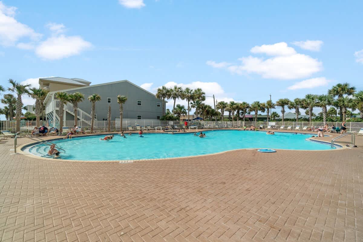 Tidewater 2615 – Swimming pool area with palm trees, surrounded by lounge chairs and people swimming.