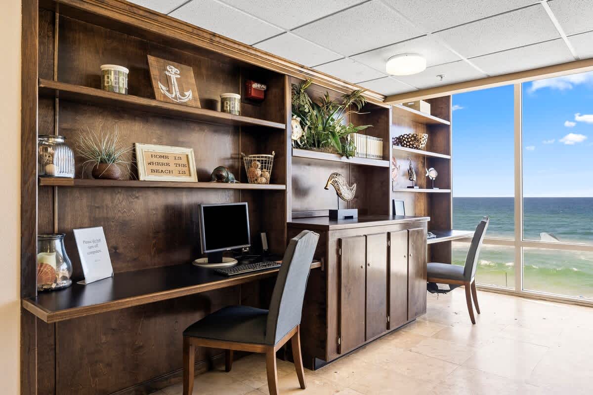 Tidewater 2615 – Home office with a desk, computer, decorative shelves, and ocean view through large windows.