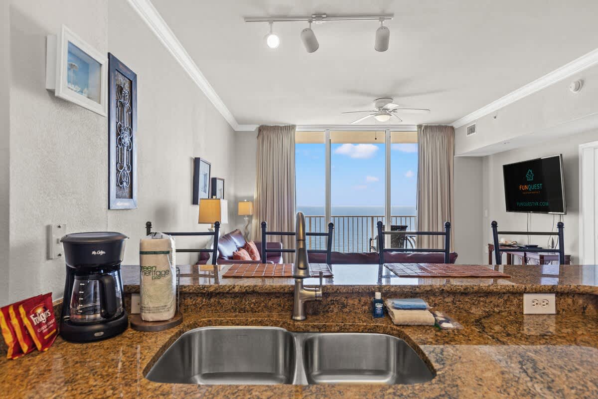 Tidewater 2615 – Living room with ocean view, kitchenette, and seating area with a couch and TV.