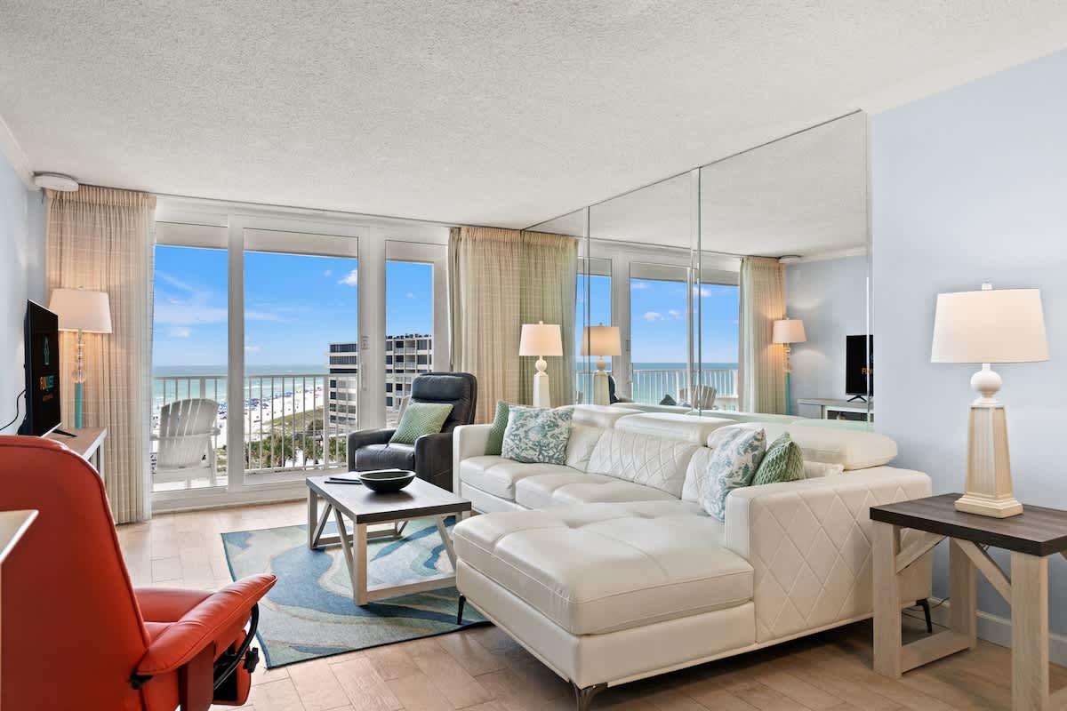 Dunes C605 – Living room with white sectional sofa, ocean view, large windows, and flat-screen TV.