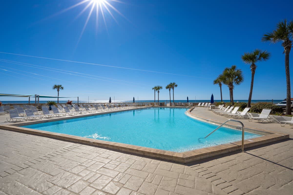 Dunes C605 – Swimming pool with lounge chairs and ocean view under a clear blue sky.