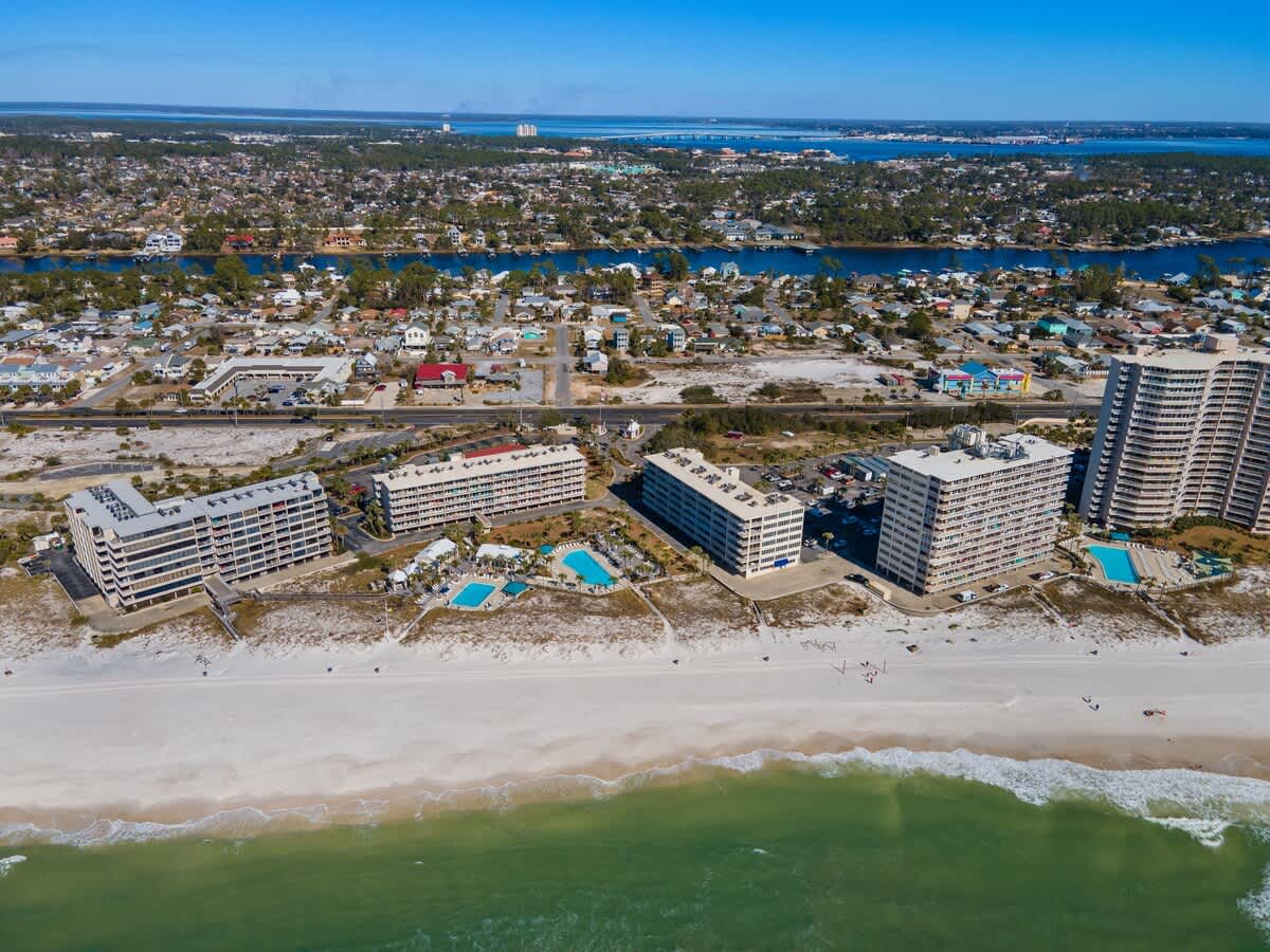 Dunes C605 – Aerial view of beachfront condos with pools and sandy beach, surrounded by residential areas and waterways.