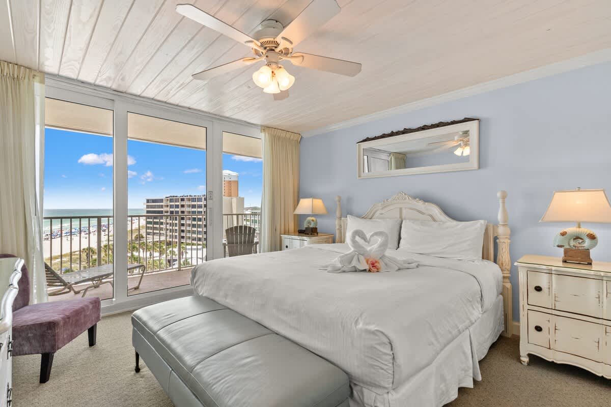 Dunes C605 – Bright bedroom with a king bed, chair, nightstand, and ocean view through large sliding glass doors.