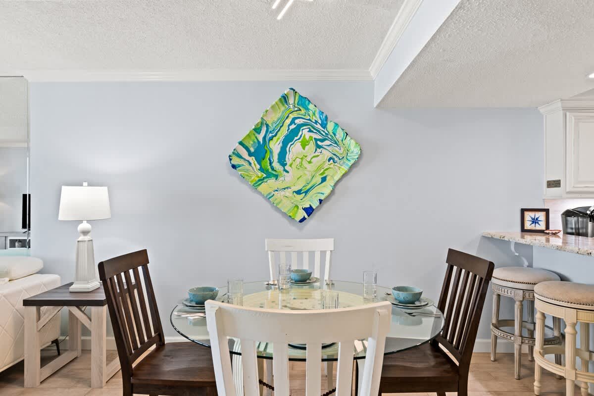 Dunes C605 – Dining area with a glass table, colorful artwork, and kitchen bar stools.