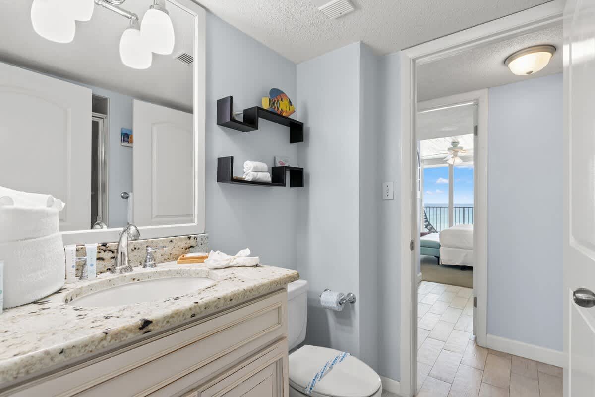 Dunes C605 – Bathroom with granite countertop, mirror, and towels; doorway leads to a bedroom with a balcony view.