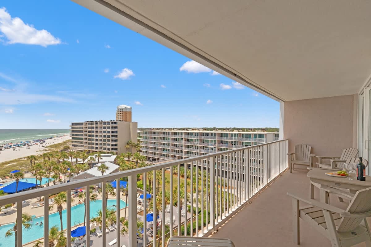 Dunes C605 – Balcony view of beach, pool area, and surrounding buildings in sunny weather.