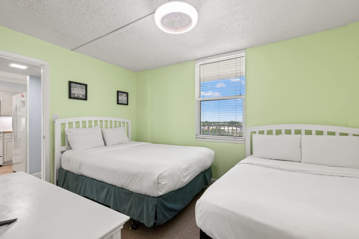 Dunes C605 – Bedroom with two beds, green walls, window view, and light fixture.