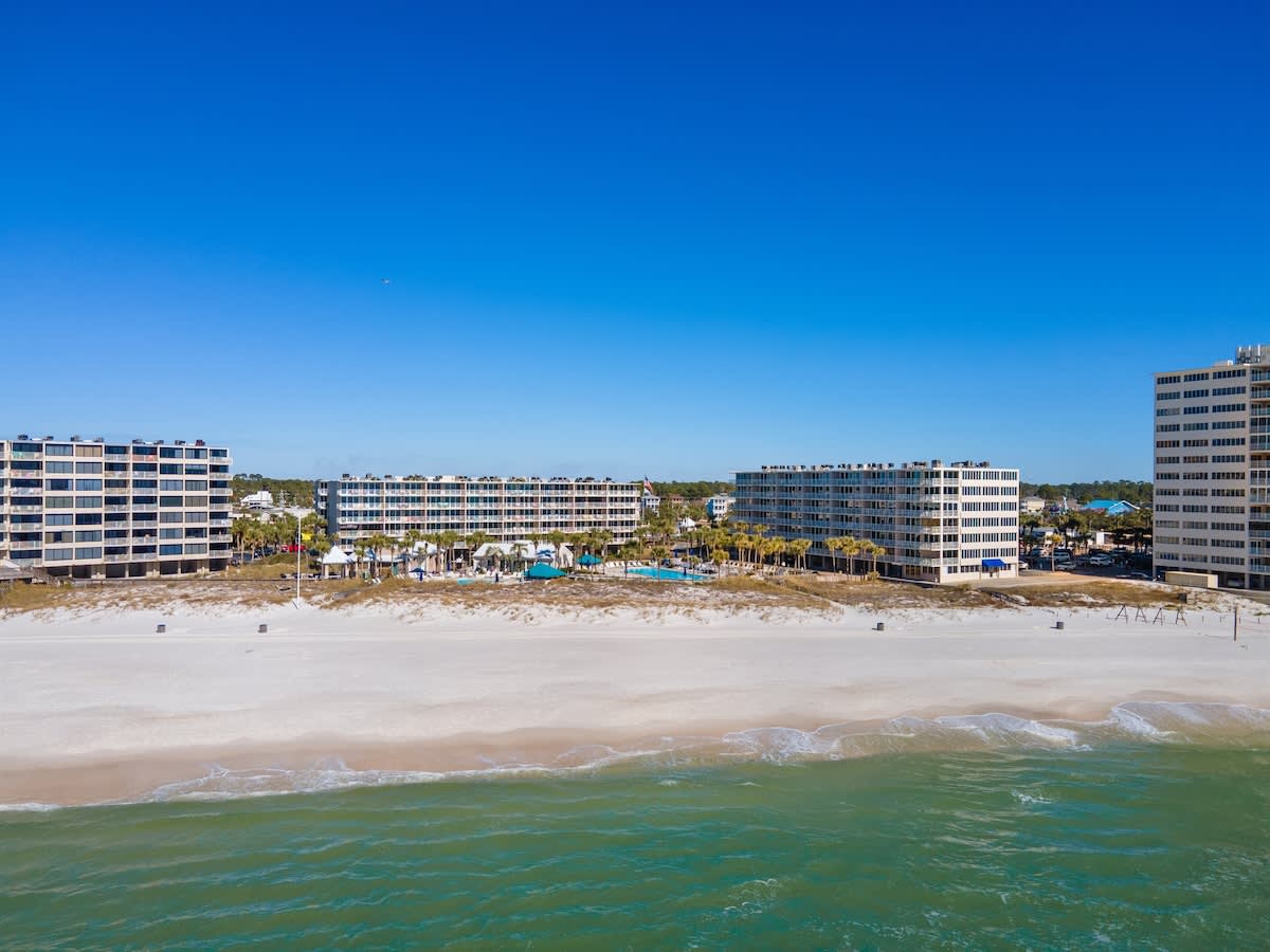 Dunes C605 – Aerial view of Dunes C605 with beachfront, surrounded by multiple condo buildings and a clear blue sky.