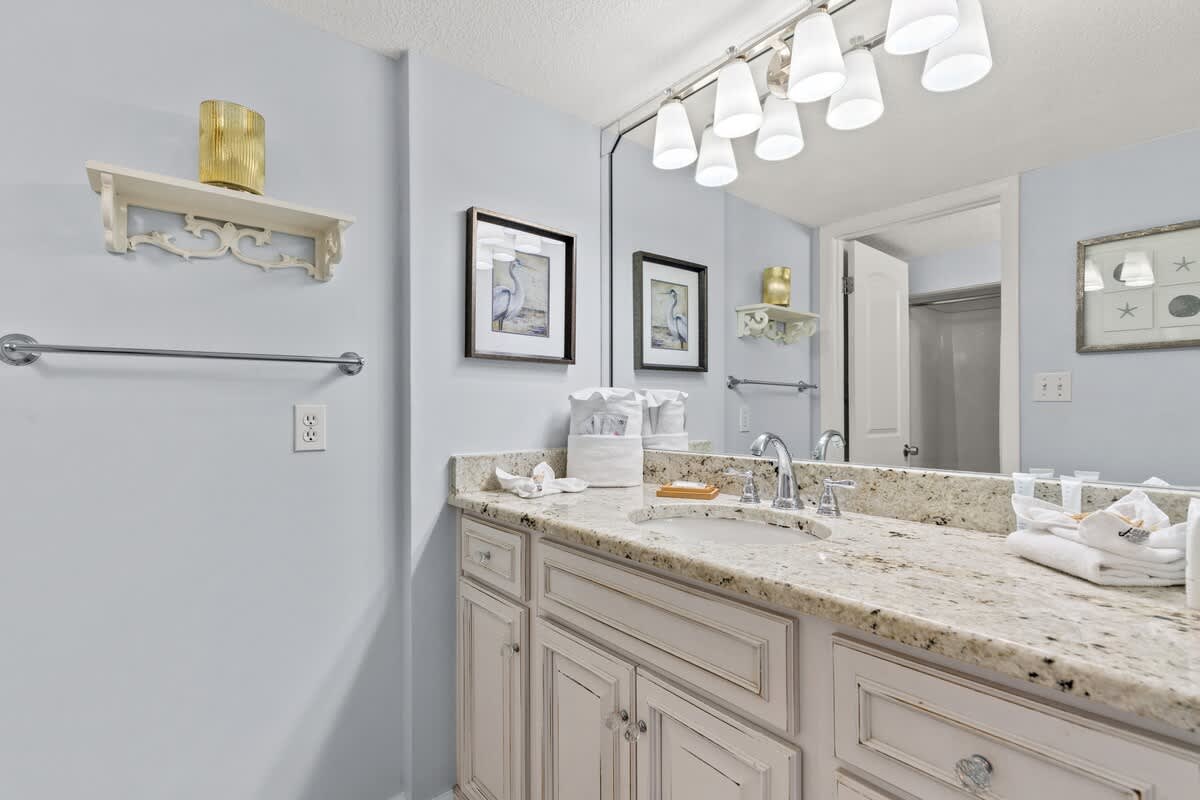 Dunes C605 – Bathroom with granite countertop, double sink, decorative shelves, and wall art.