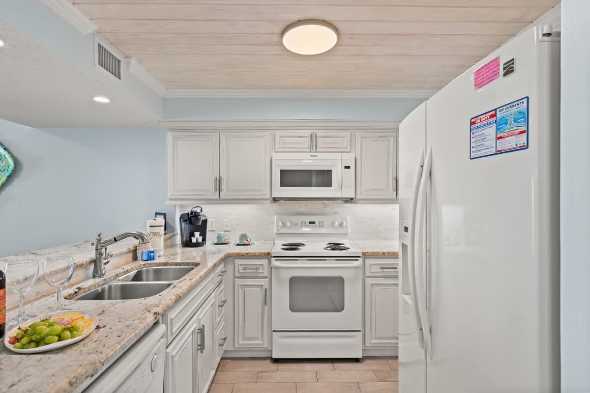 Dunes C605 – Modern kitchen with white cabinets, granite countertops, stainless steel appliances, and a coastal-themed decoration.
