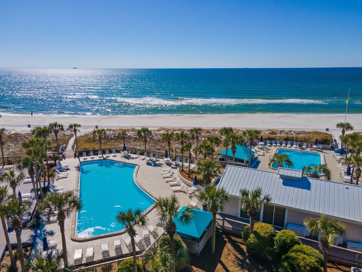 Dunes C605 – Aerial view of a pool area, palm trees, beach, and ocean in the background.