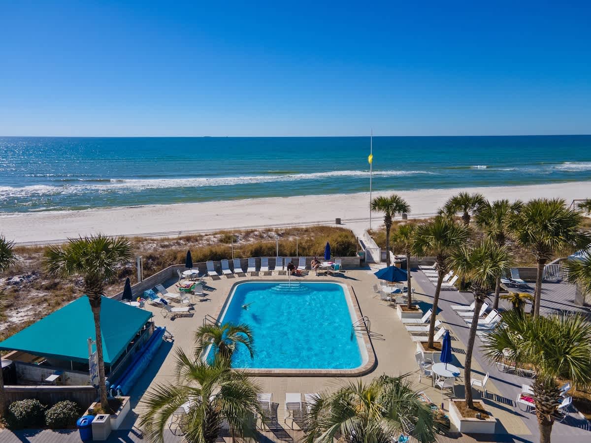 Dunes C605 – View of a beachfront pool area with lounge chairs and palm trees.