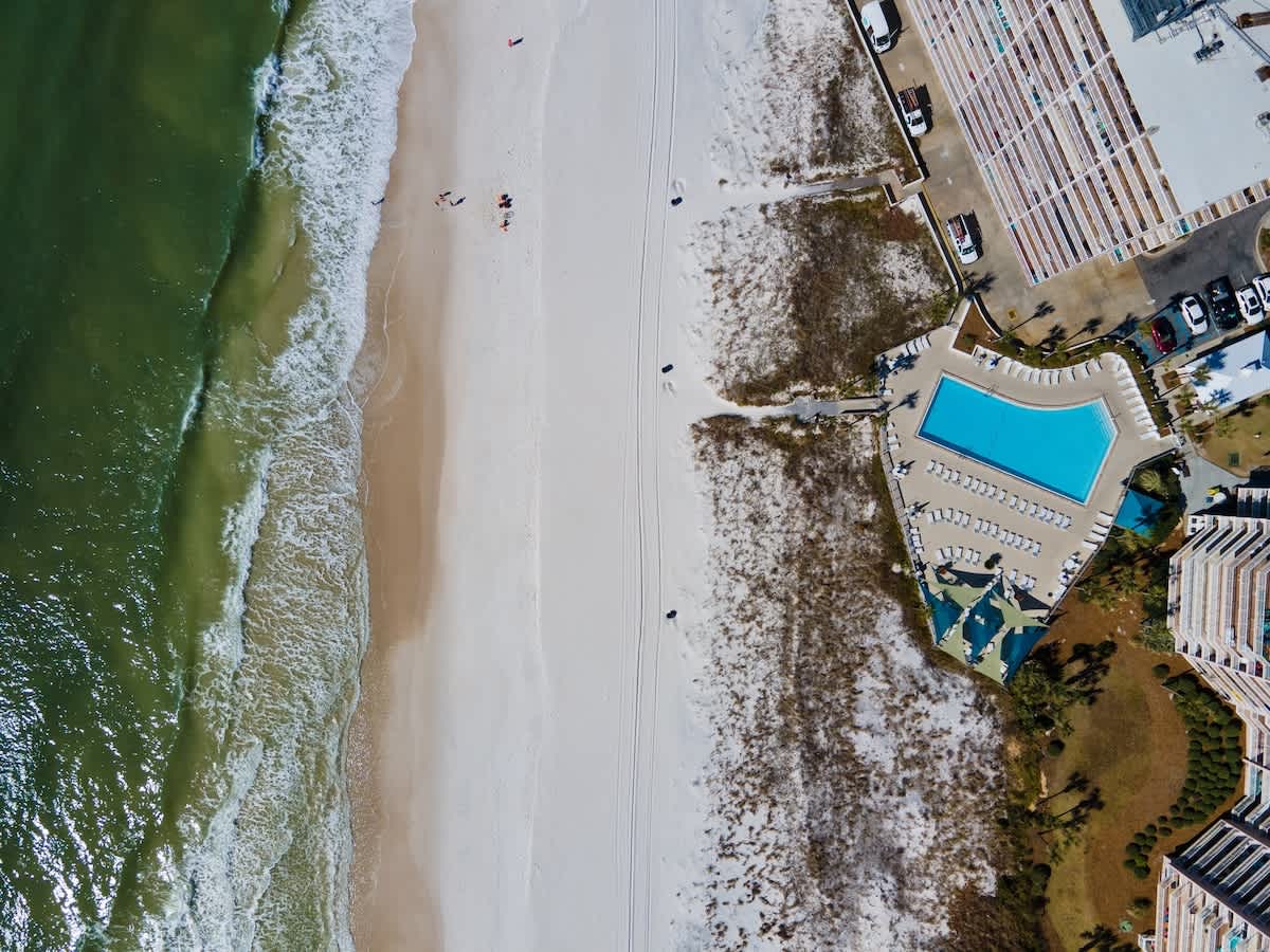 Dunes C605 – Aerial view of a beach, with a pool area and lounge chairs beside the coastline.