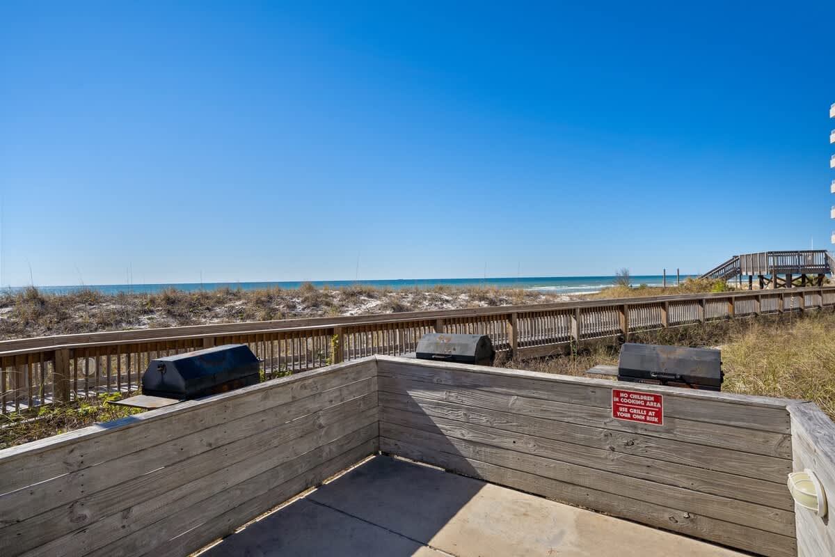 Dunes C605 – View of beach and ocean from outdoor grilling area with wooden railing.