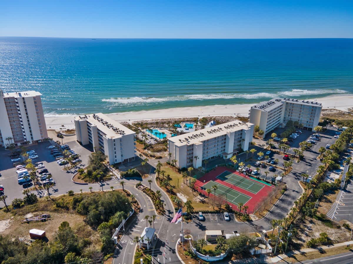 Dunes C605 – Aerial view of Dunes C605, featuring beachfront, pools, tennis courts, and surrounding palm trees.