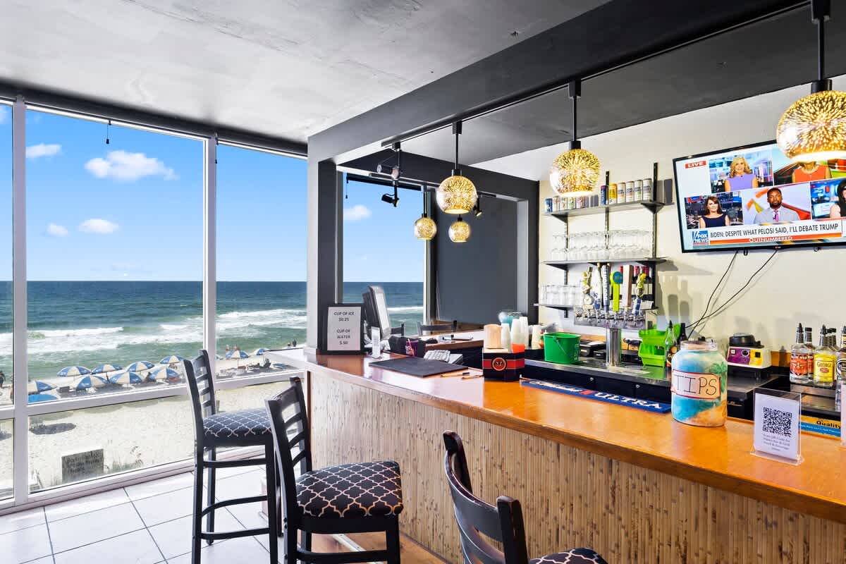 Tidewater 200 – Beachfront bar with high stools, ocean view, and shelves of drinks.