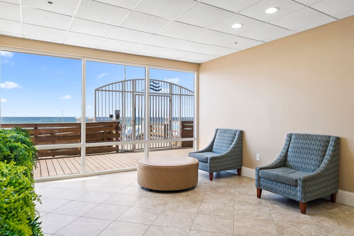 Tidewater 200 – Lounge area with two chairs, circular table, and large window overlooking wooden deck and ocean view.