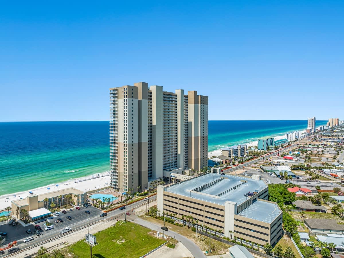 Tidewater 200 – Aerial view of Tidewater condo with ocean and beach, pools below, and nearby buildings along the coastline.