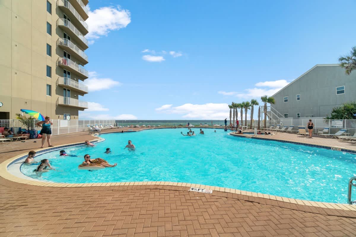 Tidewater 200 – Poolside view with people swimming, lounge chairs, and the ocean in the background.