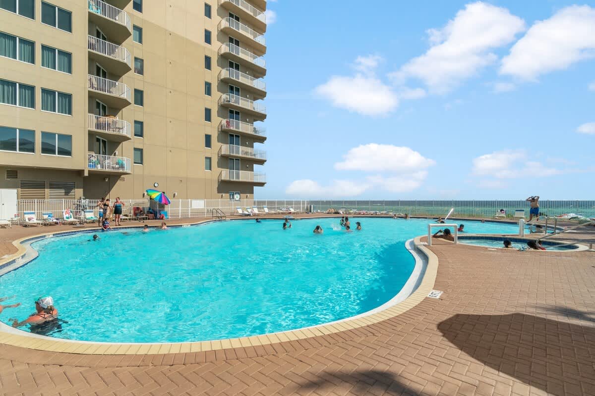 Tidewater 200 – Swimming pool area with people, lounge chairs, and ocean view in the background.