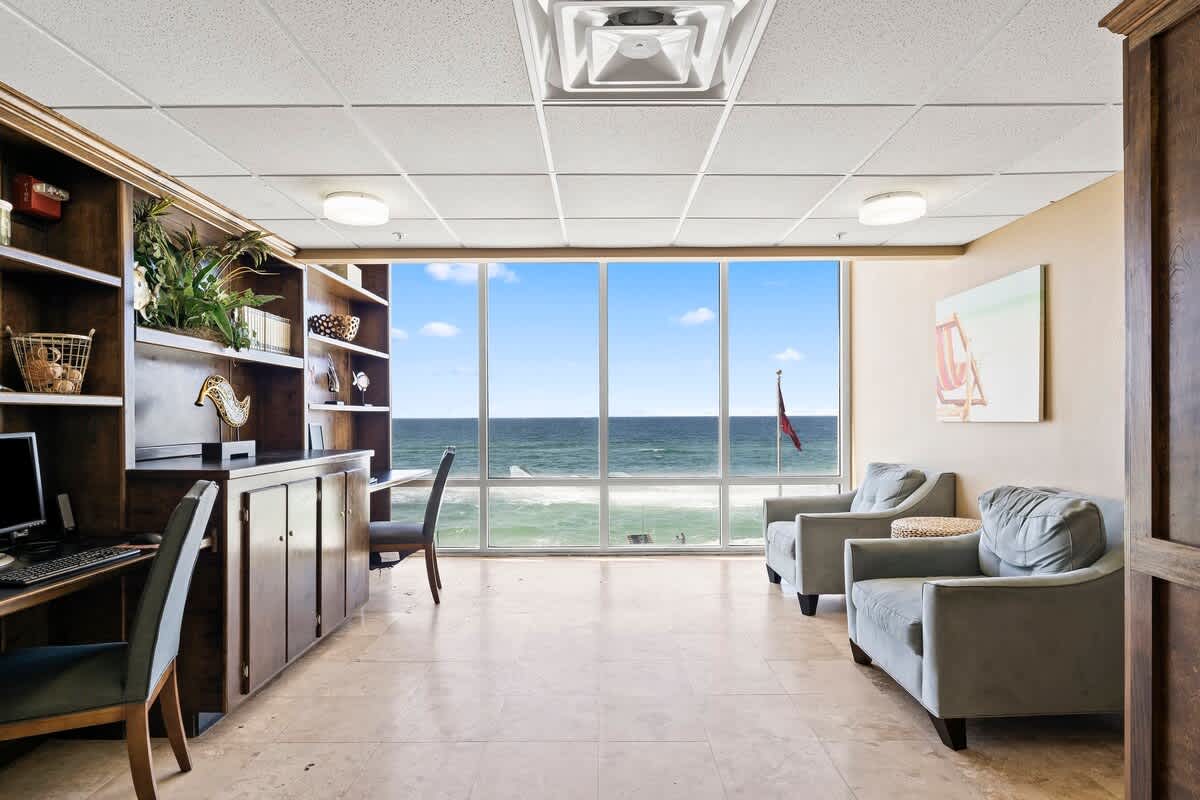 Tidewater 200 – Living area with coastal view, two chairs, desk, bookshelves, and tile flooring.