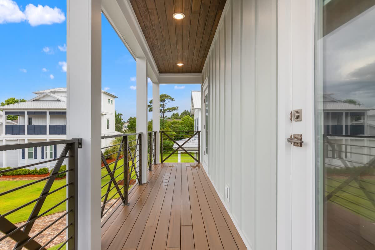 224 W Willow Mist Rd – Second-floor balcony with wooden flooring and railing, overlooking green lawn and neighboring buildings under a blue sky.