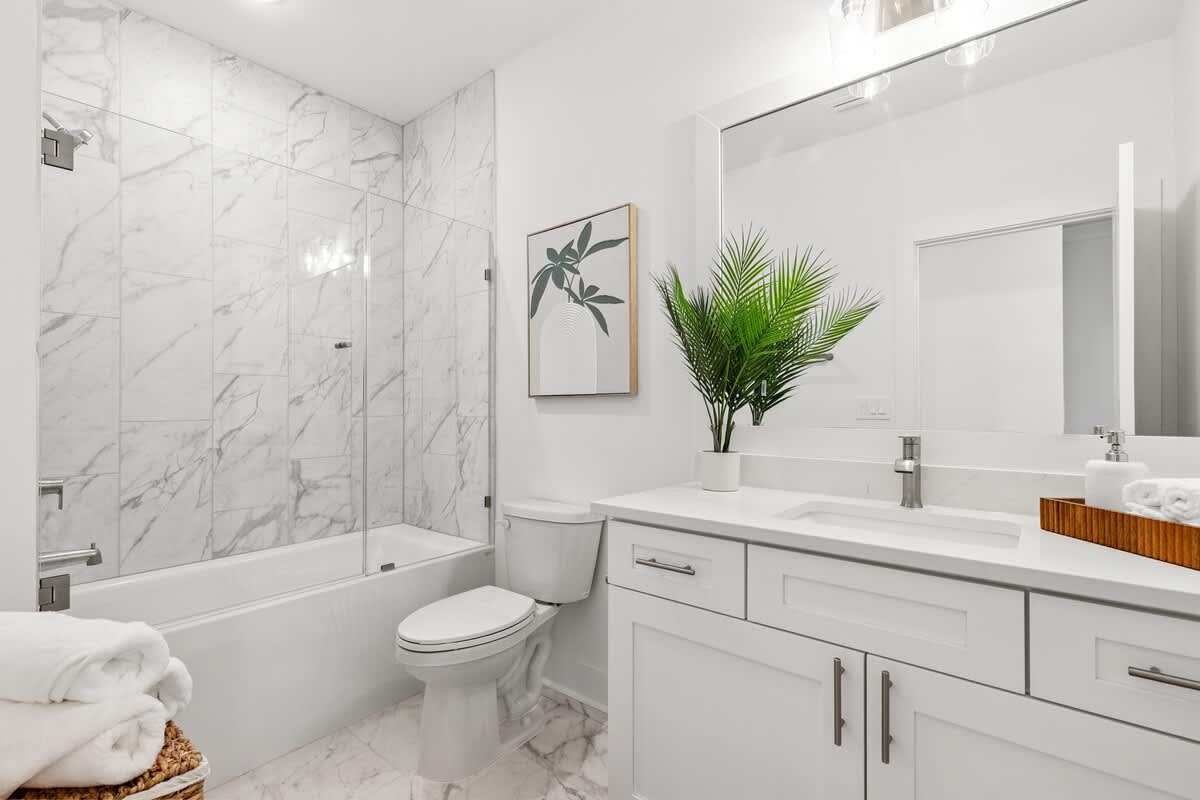 224 W Willow Mist Rd – Modern bathroom with white marble walls, a glass shower, bathtub, and large vanity with a plant.