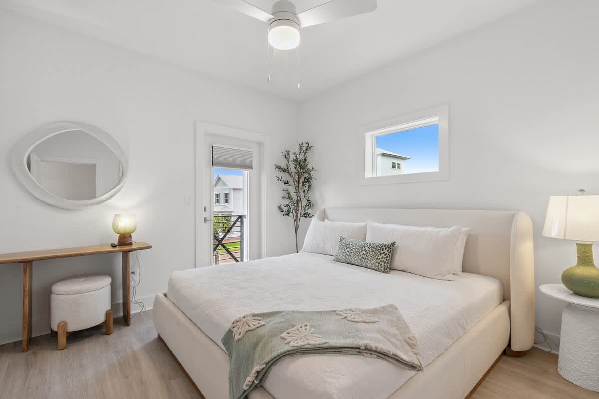 224 W Willow Mist Rd – Bright bedroom with a large bed, small table, lamp, and windows overlooking a neighboring house.