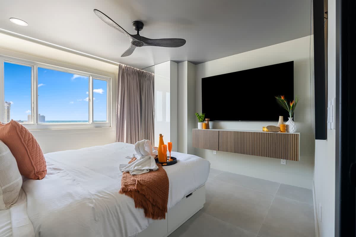 The Summit Penthouse 1501 – Bright bedroom with a king-sized bed, large windows, TV, and modern decor.