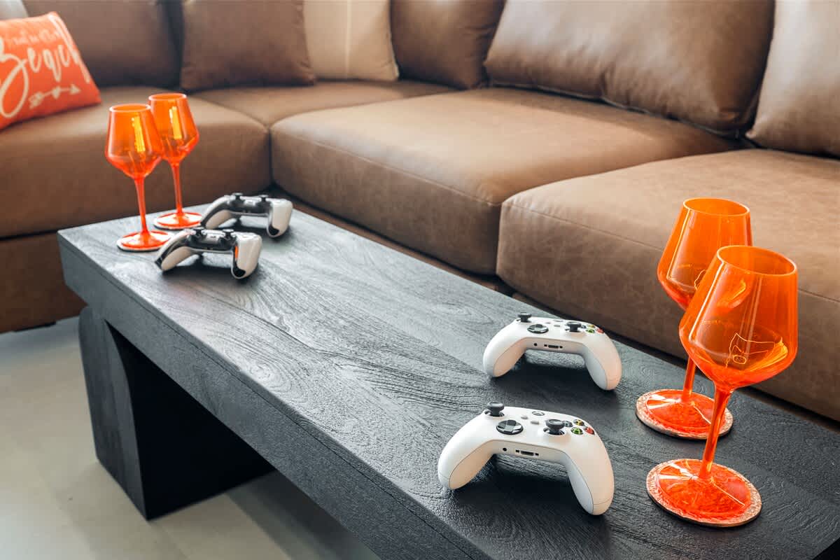 The Summit Penthouse 1501 – Living room with brown couch, black coffee table, orange glasses, and Xbox controllers.