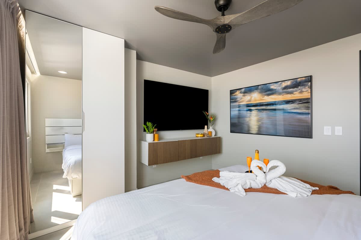 The Summit Penthouse 1501 – Modern bedroom with a large bed, wall-mounted TV, and ocean-view artwork.