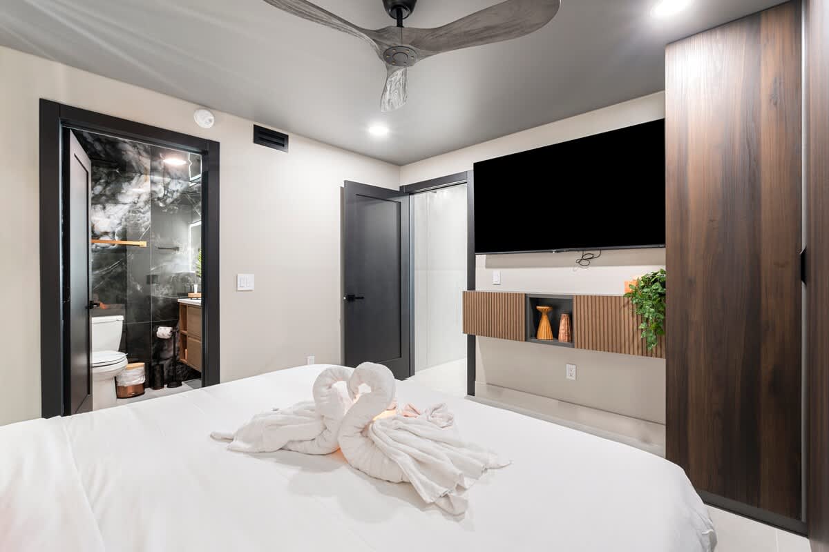 The Summit Penthouse 1501 – Modern bedroom with a queen bed, television, bathroom door, and decorative wall elements.